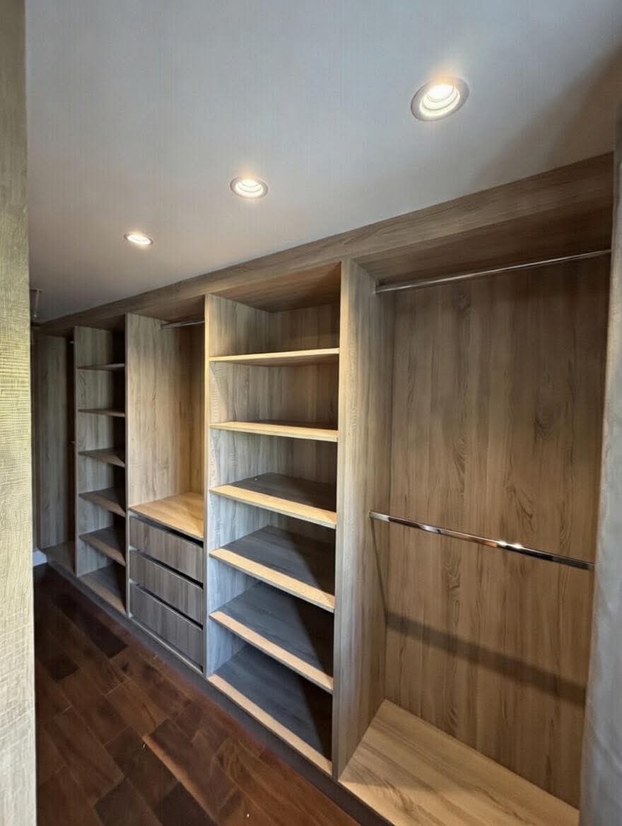 Walk-in dressing room in warm oak with open shelving, drawer bank and chrome hanging rails