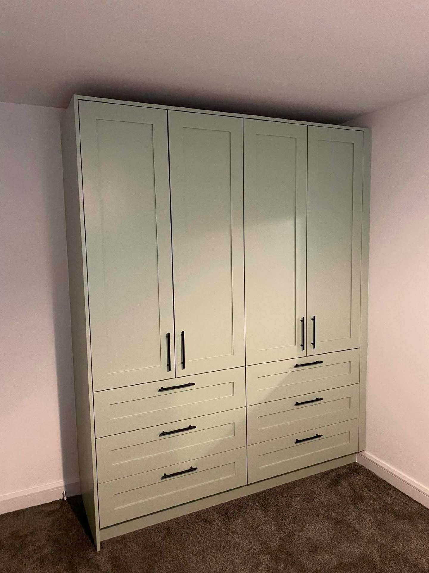 Full-height sage green shaker fitted wardrobes with four doors, six drawers and matte black bar handles